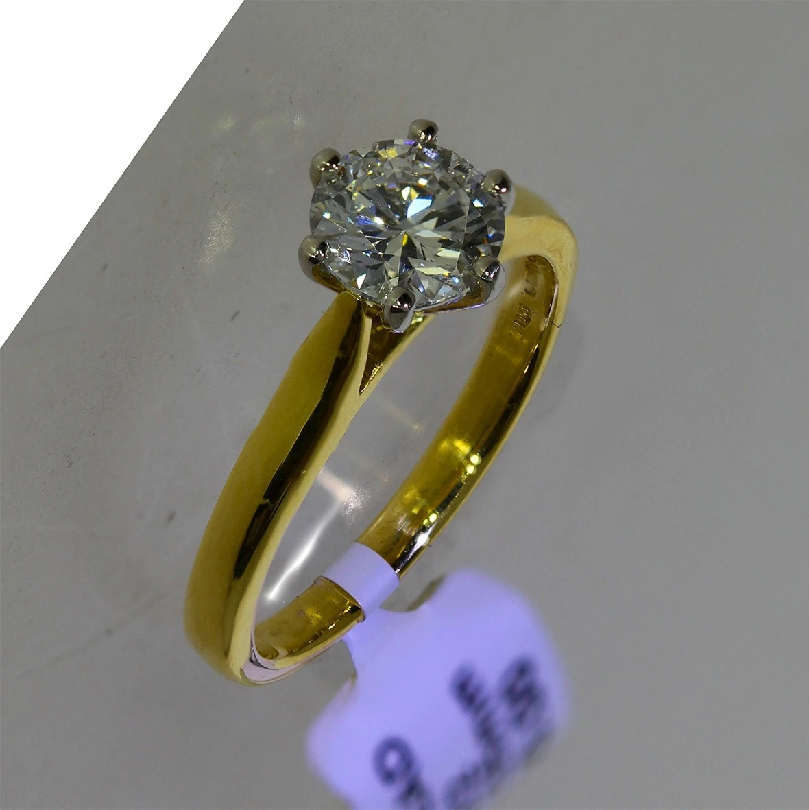 Gold solitaire ring as shot, with price tag and grey background